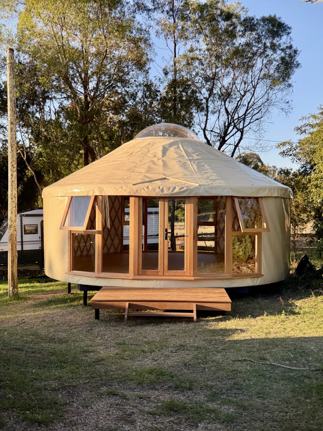 Living Yurt front entrance with open oak windows and hardwood deck at golden hour